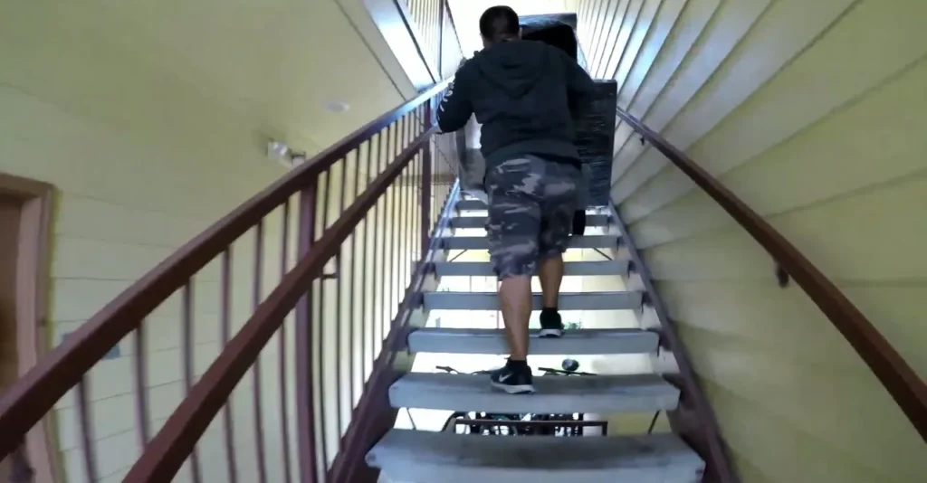 Mover carrying a wrapped piece of furniture up an apartment stairwell in Oxford, MS