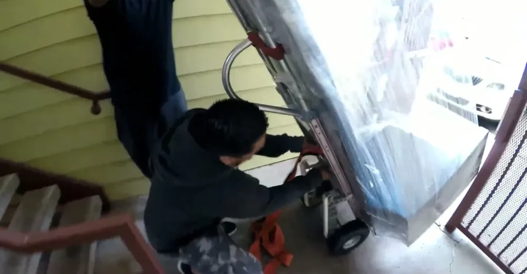 Crew strapping a wrapped item onto a hand truck at the top of the stairs
