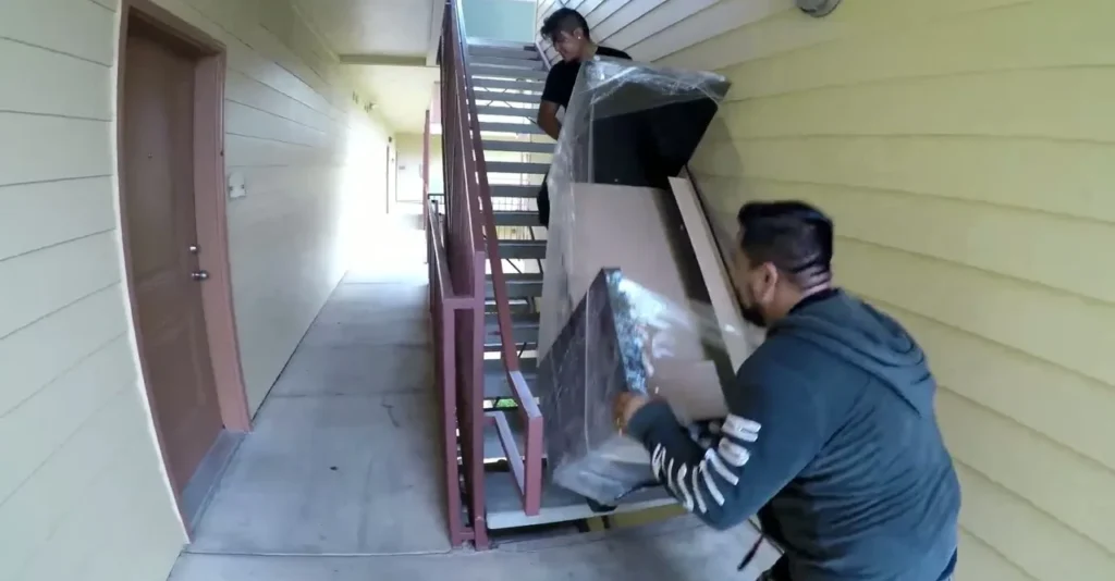 Two movers bringing wrapped furniture down an exterior stair walkway